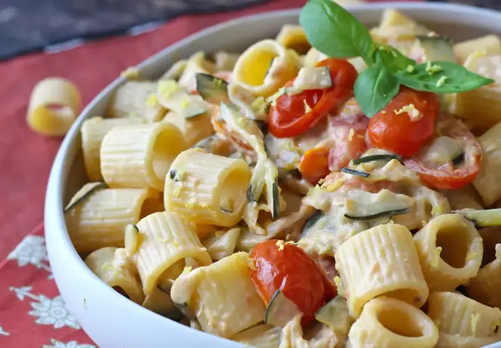 Piatto cremoso di pasta con zucchine, pomodorini e un tocco di Philadelphia, guarnito con basilico fresco.