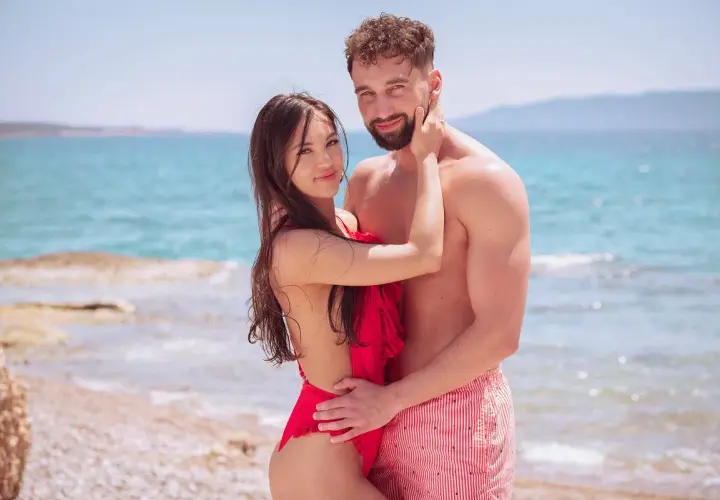 Para zakochanych na plaży, w objęciach, z morzem w tle. Ich spojrzenia mówią wszystko, bo love never lies.