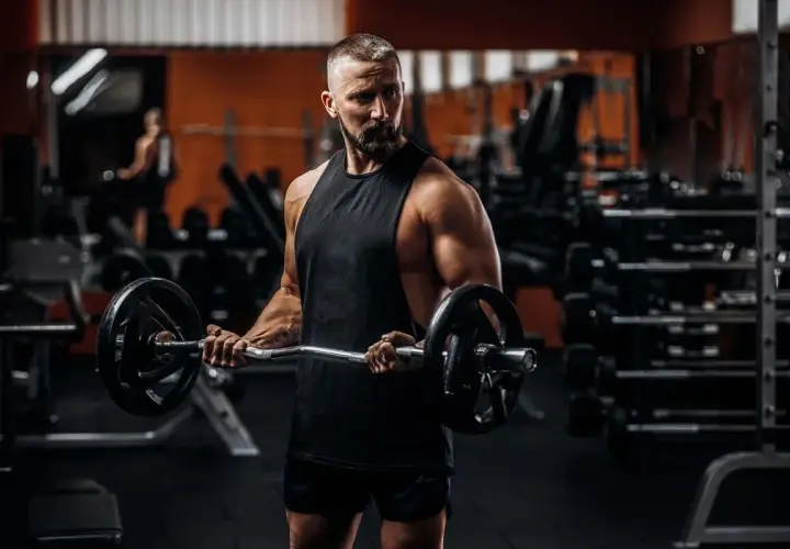 Mężczyzna z brodą ćwiczy biceps z gryfem. To inspiracja do odchudzania po 40.