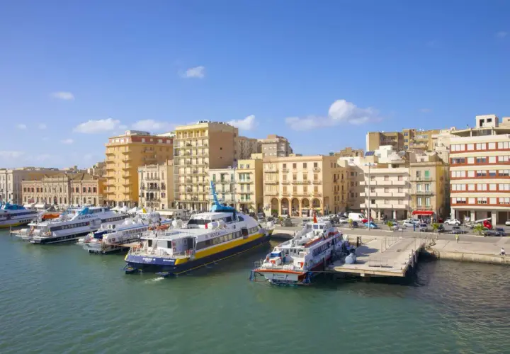 Ferries docked in a harbor, with buildings lining the waterfront. Wondering if you can drive to Sicily? These ferries might be your answer!
