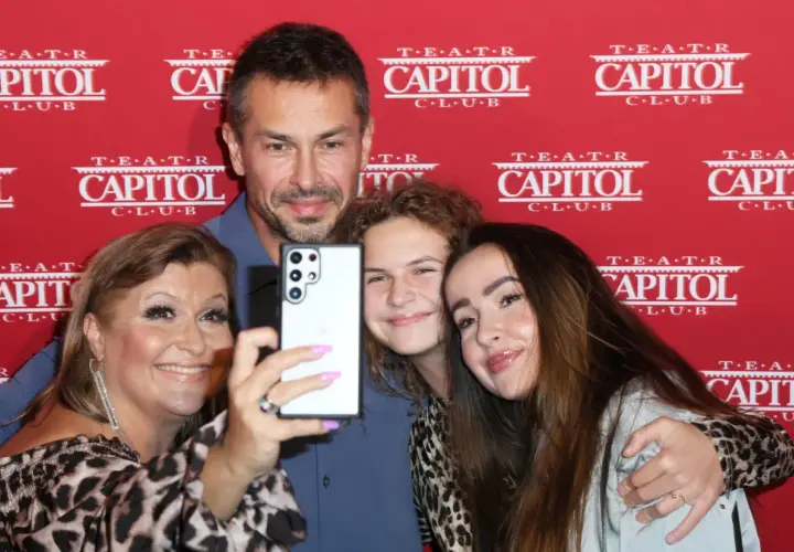 Katarzyna Skrzynecka z rodziną robi selfie. Uśmiechnięci rodzice i ich dzieci pozują na tle czerwonego banera z napisem "Teatr Capitol".
