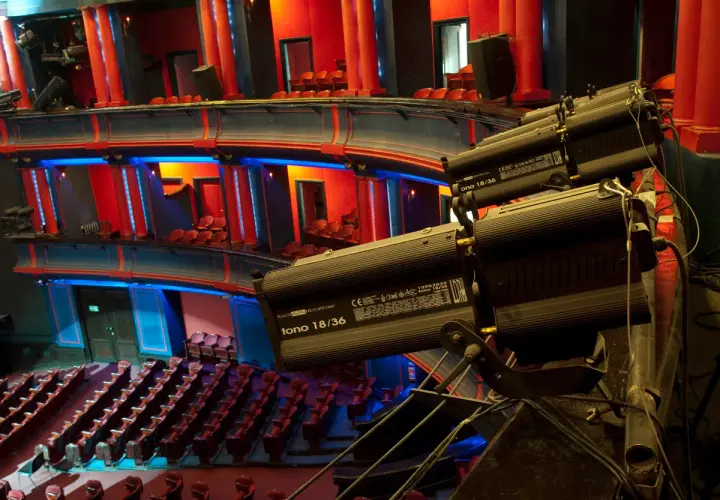 Wnętrze teatru z rzędami czerwonych siedzeń i balkonami. Reflektory oświetlają scenę. Ile miejsc ma teatr roma?