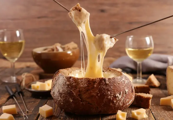 Un pain creusé sert de bol pour une fondue au vin blanc dégoulinante. Des morceaux de pain et de fromage sont prêts à être trempés.