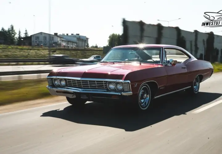 Czerwony Chevrolet Impala 1967 sunie po drodze, błyszcząc w słońcu. Klasyk w ruchu.