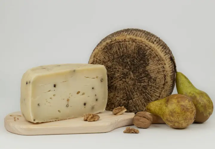 Varietà di tipi di pecorino, uno a spicchio con pepe nero, uno intero con crosta scura, pere e noci su tagliere di legno.