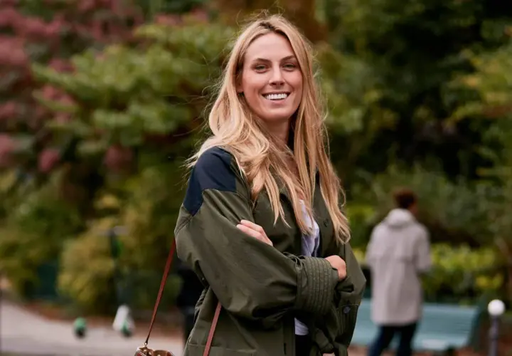Mujer sonriente con un corte de pelo a capas, luciendo una chaqueta verde y un bolso de cuero.