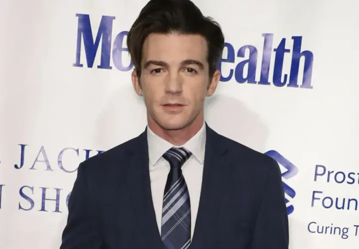 Drake Bell w garniturze, znany z filmów, seriali i programów, pozuje na tle wydarzenia charytatywnego.