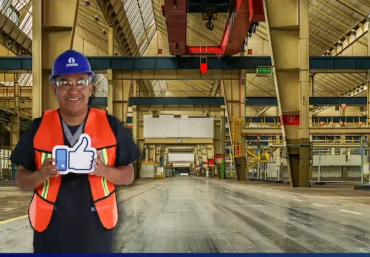 Hombre con casco y chaleco naranja sonríe en una nave industrial, sosteniendo un pulgar hacia arriba. Sus sistemas de limpieza son eficientes.