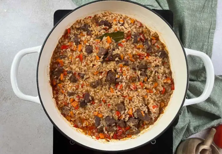 Arroz con carne y verduras, cocinado en una olla blanca. Los trozos de carne se mezclan con el arroz y pimientos rojos y zanahorias picadas.