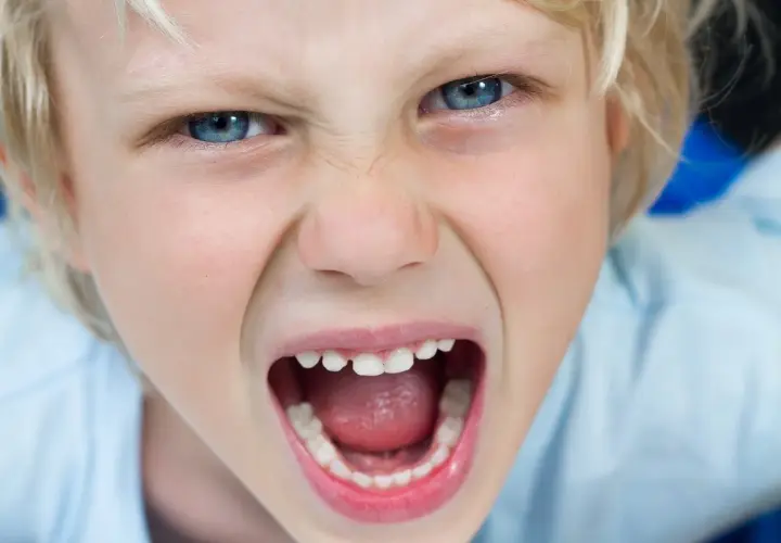 Niño con ojos azules muy abiertos y boca gritando, mostrando una expresión de enojo que podría indicar un trastorno negativista desafiante.