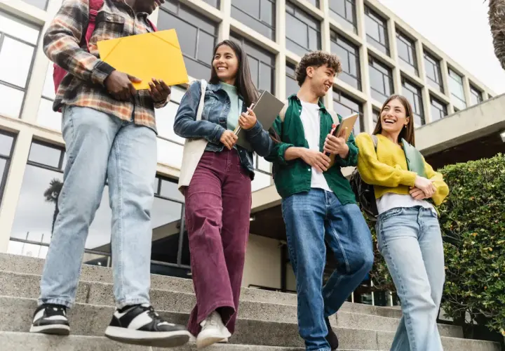 Grupa studentów schodzi po schodach, niosąc książki i teczki. Ich uśmiechy sugerują, że są gotowi na wyzwania, niczym w ramach obrony cywilnej.