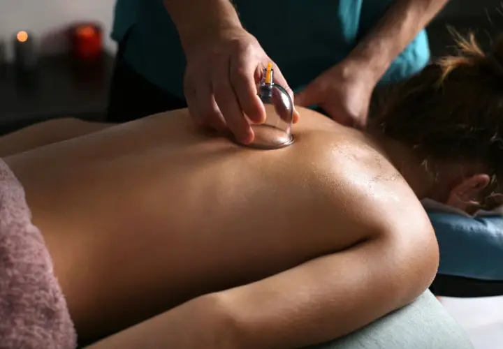 Un praticien applique une ventouse pour un drainage lymphatique du dos. La peau est huilée, créant un effet lumineux.