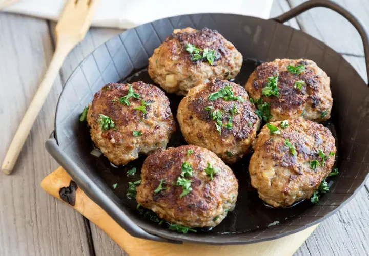 Sechs goldbraune Fleischpflanzerl, garniert mit Petersilie, in einer Pfanne. Ein leckeres Fleischpflanzerl Rezept zum Nachkochen.