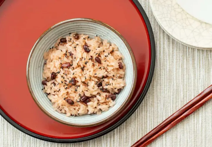 A bowl of Japanese red bean rice, sprinkled with black sesame seeds, sits on a red tray.