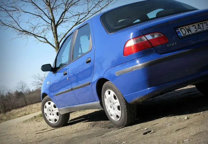 Niebieski Fiat Albea na tle drzew i błękitnego nieba.