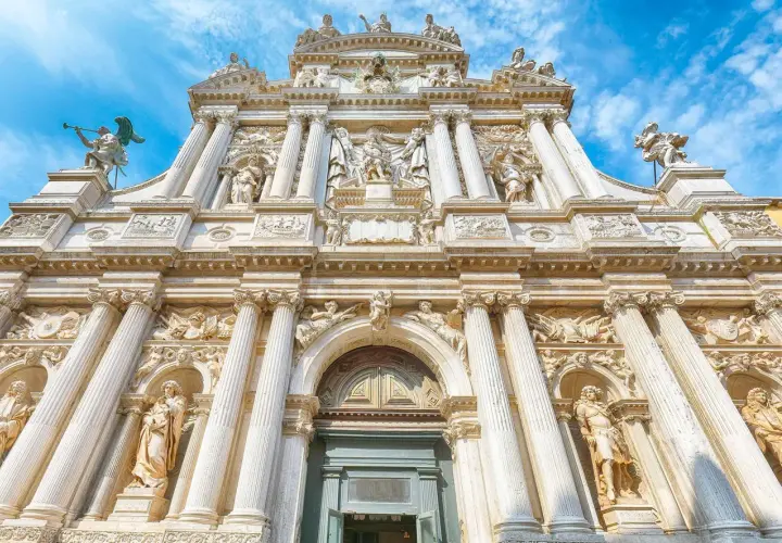Façade baroque de Santa Maria del Giglio à Venise, ornée de statues et de colonnes imposantes sous un ciel bleu.