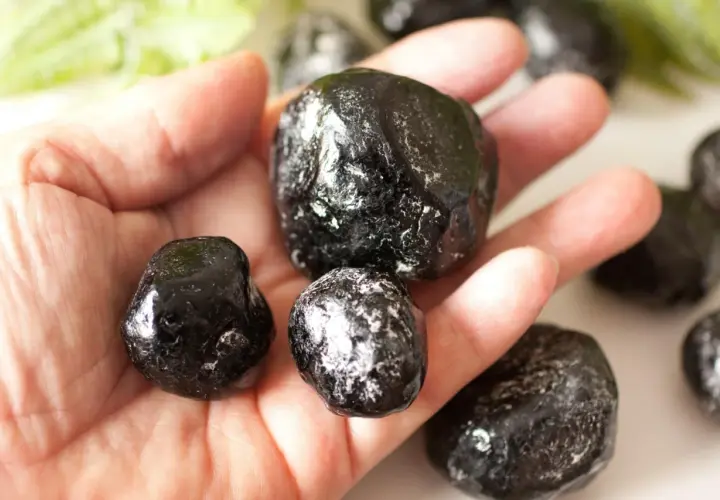 Eine Hand hält mehrere glänzende, schwarze Apachentränen-Steine. Sie sehen aus wie kleine, dunkle Tropfen.