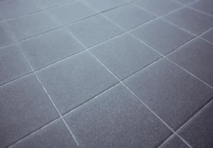 Dettaglio di piastrelle grigie con fughe pavimento pulite e uniformi, che creano un motivo geometrico ordinato.
