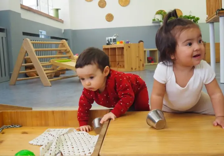 Bebés explorando en una **montessori guarderia**. Un niño gatea con un suéter rojo, mientras otro sonríe.