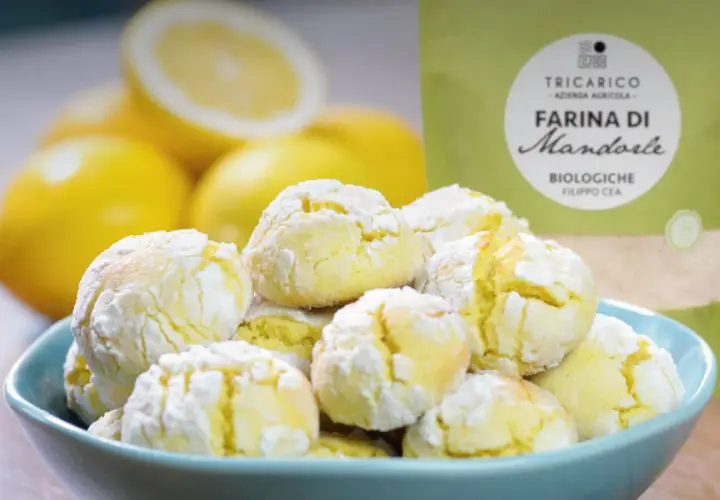 Biscotti con farina di mandorle, morbidi e profumati, accanto a limoni freschi e una confezione di farina.