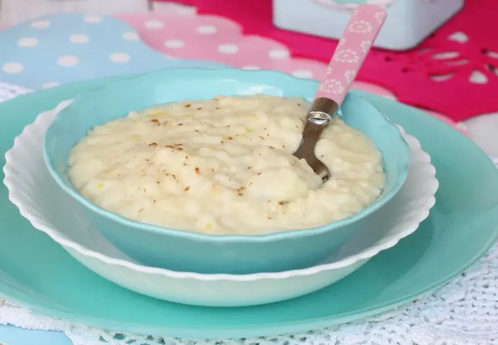 Un cremoso riso e latte, cosparso di cannella, servito in una ciotola azzurra con un cucchiaino rosa.