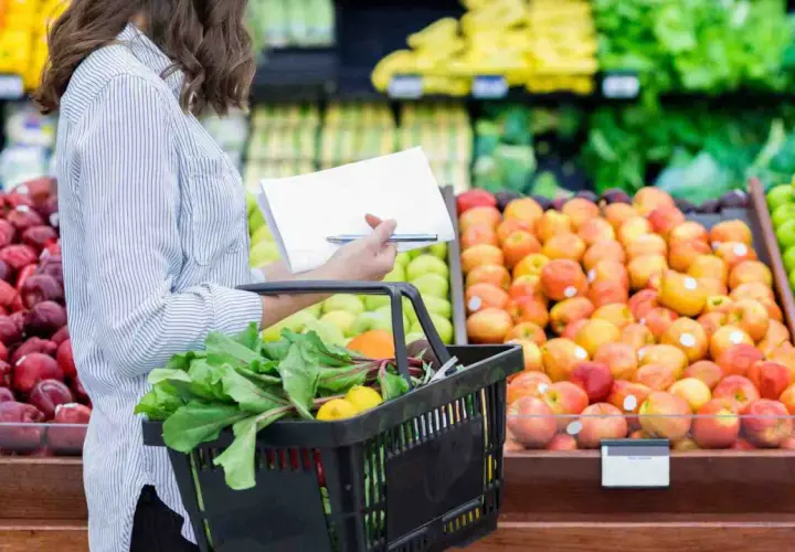 Donna con lista della spesa sceglie verdure fresche e frutta colorata al supermercato.
