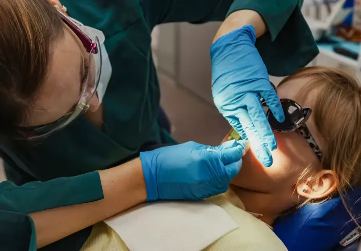 Dentystka wykonuje lakowanie zębów u dziecka. Sprawdź, jaka jest lakowanie zębów cena i zadbaj o uśmiech swojej pociechy.