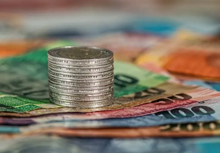 Stos monet na tle kolorowych banknotów.