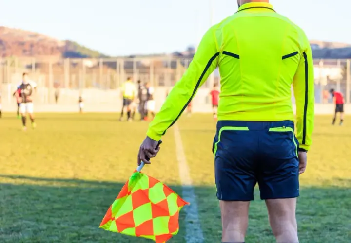 Sędzia liniowy z chorągiewką w ręku, gotowy do oceny akcji na boisku. Każdy mecz to szansa na zdobycie punktów do rankingu UEFA.