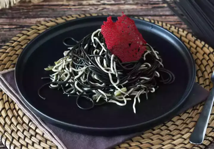 Spaghetti neri e bianchi, un contrasto elegante. Il nero di seppia dona un sapore unico a questo piatto, guarnito con una cialda rossa croccante.