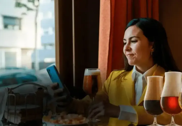Donna con smartphone e bicchieri di birra. Scopri come si può comprare il birg online per gustarlo comodamente.