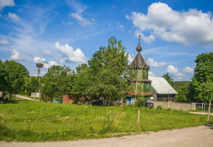 Zielona cerkiew, symbol tradycji starowierców w Polsce, na tle błękitnego nieba z chmurami. Bociany w gnieździe na słupie.