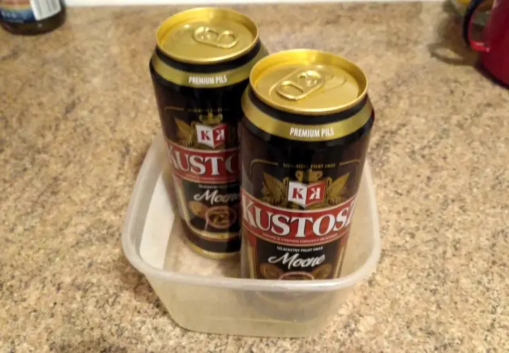 Dwa puszki piwa Kustosz Premium Pils w plastikowym pojemniku. Idealne na wieczór z dobrym **kustosz piwo**.