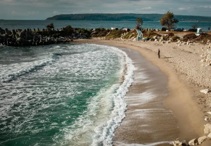 Plaża w Bułgarii, gdzie morze szumi, a fale obmywają brzeg. W oddali widać wzgórza i samochody.