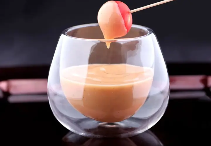 Une tomate cerise trempée dans une sauce cocktail onctueuse, servie dans un verre élégant.