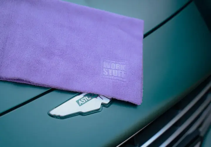 Fioletowy ręcznik z mikrofibry z logo Work Stuff leży na zielonym samochodzie Aston Martin. Dowiedz się, jak prać ręcznik z mikrofibry, by służył latami.