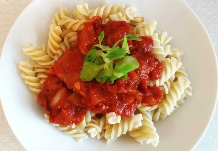 Fusilli con la mejor salsa de tomate italiana, cubierta con una hoja verde fresca.