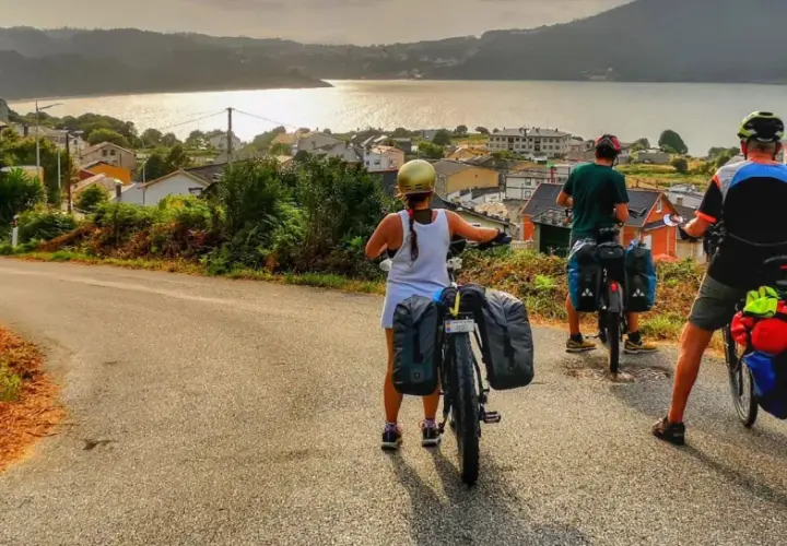 Ciclistas con alforjas exploran **rutas bicicleta** con vistas a un pueblo costero y el mar al atardecer.