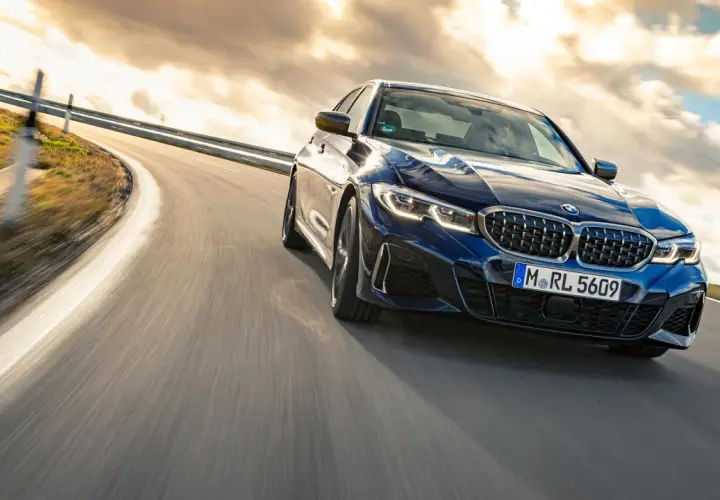 Blauer BMW M340i fährt auf einer kurvigen Straße bei Sonnenuntergang.