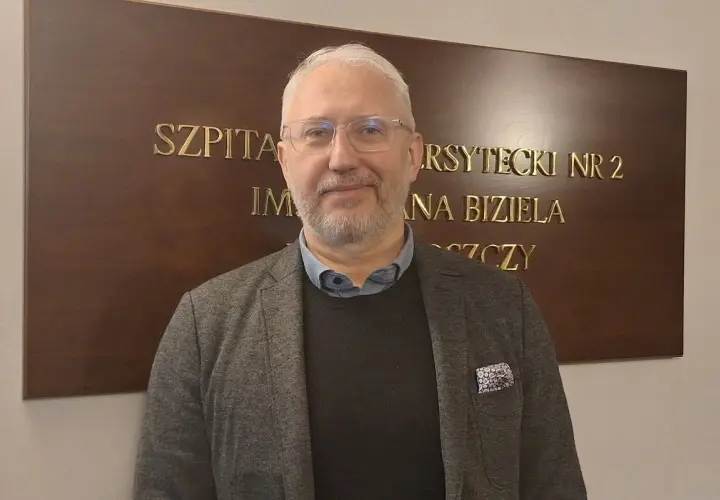Mężczyzna w okularach i marynarce stoi przed tablicą z napisem "SZPITAL UNIWERSYTECKI NR 2 IM. JANA BIZIELA BYDGOSZCZ".