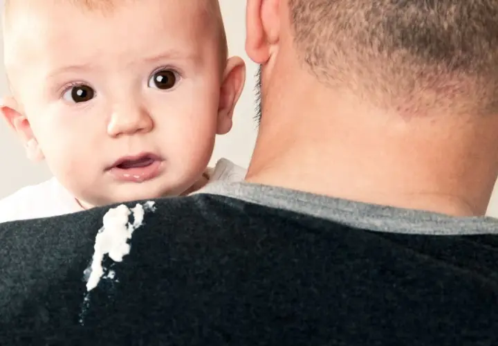 Un neonato di 1 mese ha un rigurgito, lasciando una macchia sul maglione del padre.