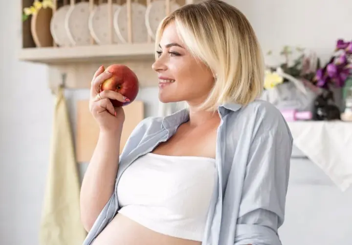 Kobieta w ciąży trzyma jabłko, zastanawiając się, co jeść żeby zajść w ciążę. Zdrowa dieta to podstawa.