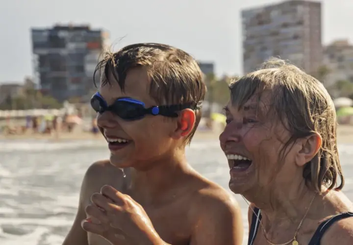 Chłopiec w goglach i starsza kobieta śmieją się na plaży. Wakacje bez zmartwień dzięki najlepszemu ubezpieczeniu turystycznemu.