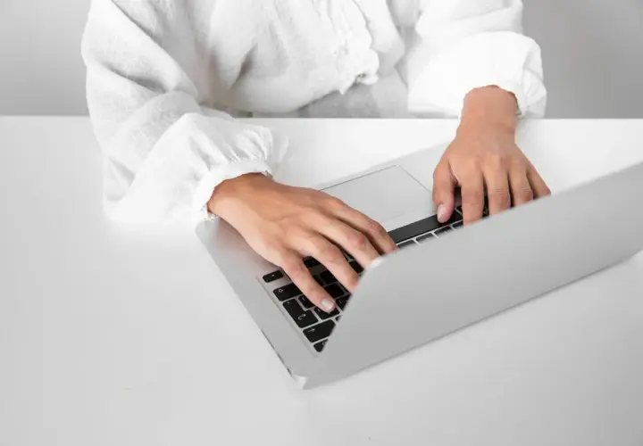Dłonie piszą na laptopie, przygotowując zaświadczenie o niezaleganiu.