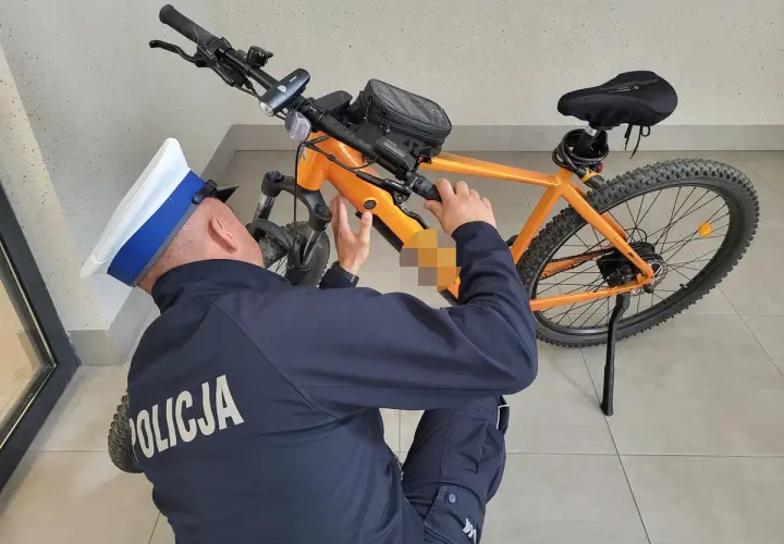 Policjant w czapce bada pomarańczowy rower elektryczny, próbując zrozumieć, jak działa rower elektryczny.