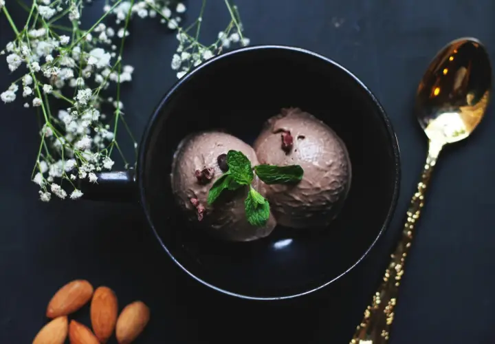Deux boules de glace à la figue, garnies de menthe fraîche, dans un bol noir, avec des amandes et une cuillère dorée.