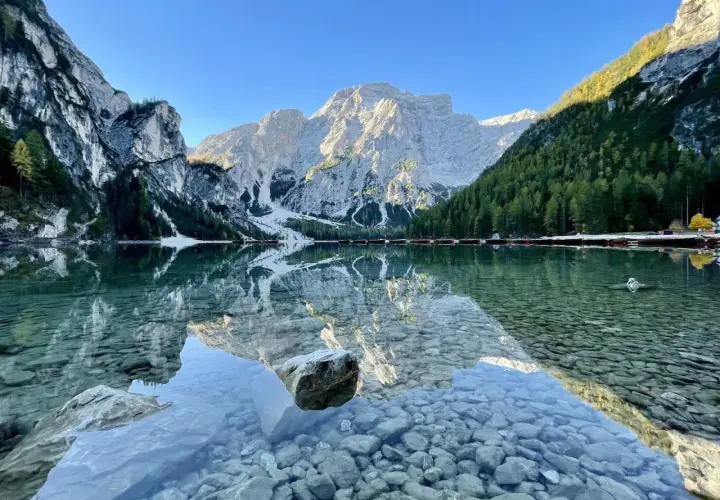 Der Pragser Wildsee spiegelt majestätische Berge und grüne Wälder. Kleine Boote liegen am Ufer.