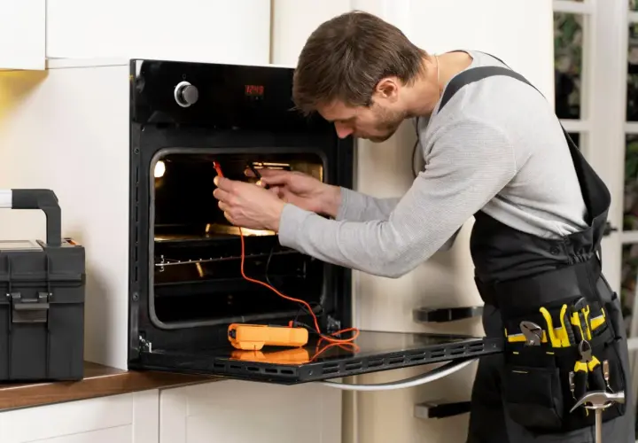 Technik sprawdza, czy piekarnik elektryczny ma bezpiecznik, używając multimetru. Obok stoi skrzynka z narzędziami.