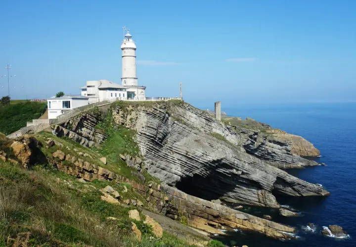 El faro de Cabo Mayor se alza sobre acantilados rocosos, vigilando el azul mar Cantábrico.