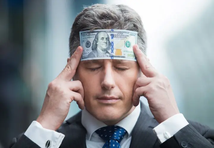 Biznesmen z banknotem 100 dolarów na czole, zamyślony nad tym, jak pomnażać pieniądze.